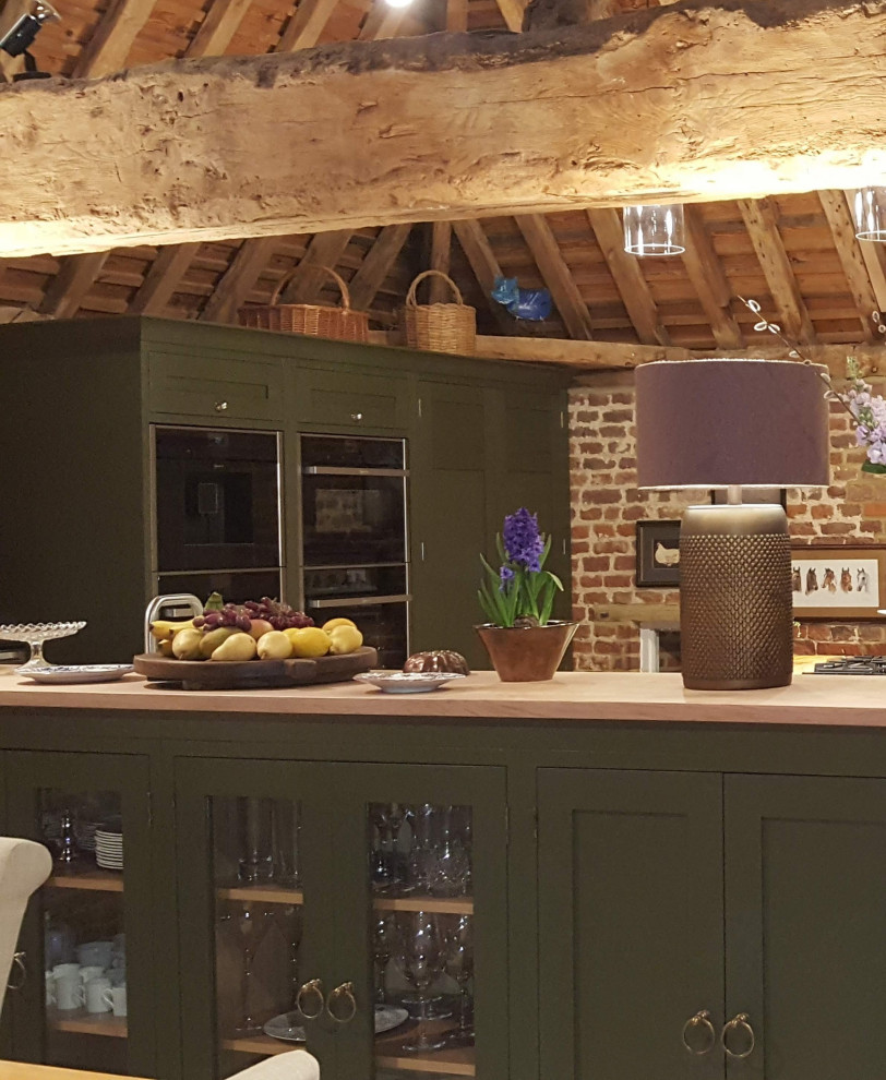 Photo of a medium sized eclectic open plan kitchen in Buckinghamshire with shaker cabinets, green cabinets, engineered stone countertops, black appliances, a vaulted ceiling and feature lighting.
