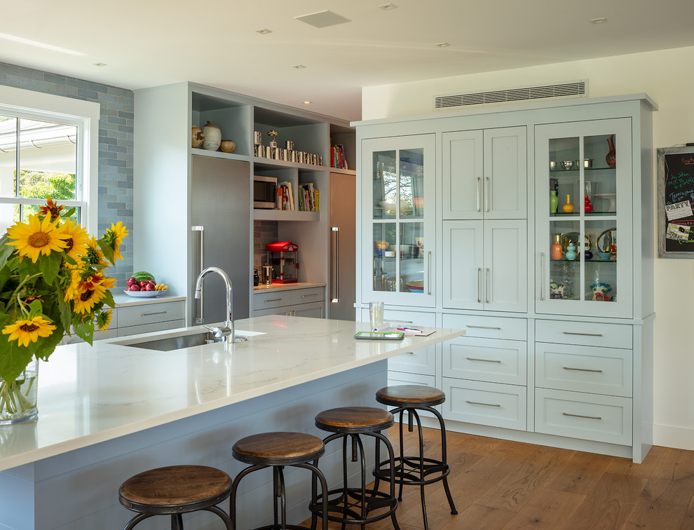 This is an example of a mid-sized beach style galley kitchen in Other with an undermount sink, blue cabinets, blue splashback, stainless steel appliances, medium hardwood floors, with island, white benchtop, quartz benchtops, ceramic splashback and brown floor.