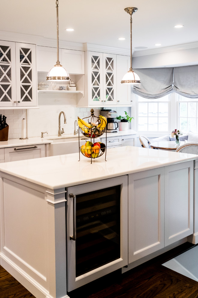 Mid-sized transitional dark wood floor and brown floor enclosed kitchen photo in New York with a farmhouse sink, recessed-panel cabinets, white cabinets, quartzite countertops, white backsplash, subway tile backsplash, stainless steel appliances and an island