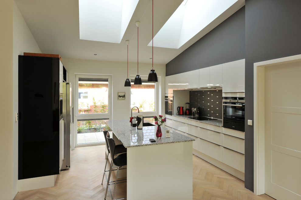 Inspiration for a large contemporary galley separate kitchen in Other with an undermount sink, flat-panel cabinets, white cabinets, multi-coloured splashback, light hardwood floors, with island and granite benchtops.