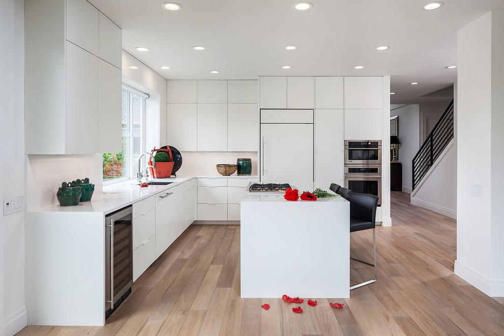 Design ideas for a contemporary l-shaped kitchen in Portland with flat-panel cabinets, white cabinets, quartz benchtops, white splashback, light hardwood floors, with island, an undermount sink and panelled appliances.