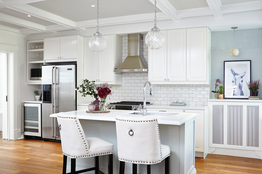 Mid-sized traditional eat-in kitchen in Toronto with an undermount sink, raised-panel cabinets, white cabinets, white splashback, subway tile splashback, stainless steel appliances, medium hardwood floors, with island and quartz benchtops.