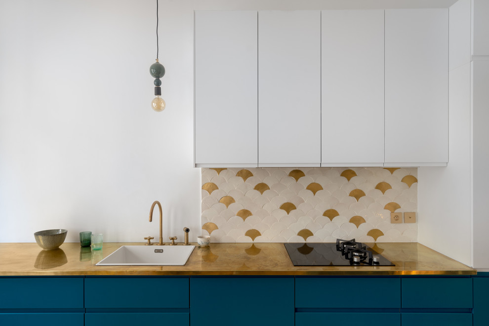 This is an example of a mid-sized scandinavian galley open plan kitchen in Paris with a single-bowl sink, beaded inset cabinets, blue cabinets, copper benchtops, white splashback, ceramic splashback, black appliances, light hardwood floors, no island, brown floor and yellow benchtop.