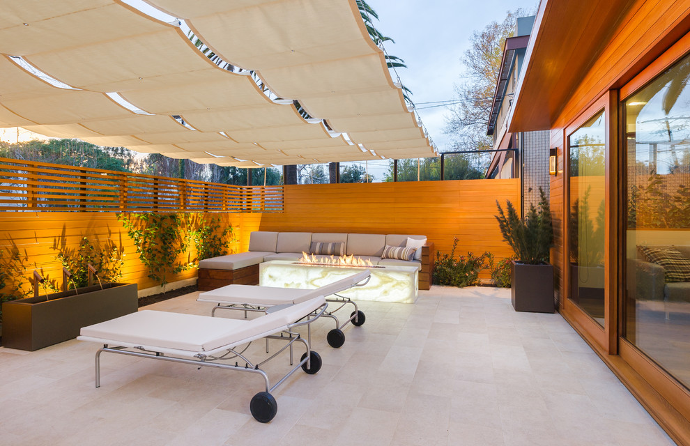Photo of a mid-sized modern patio in Los Angeles with a fire feature, tile and an awning.