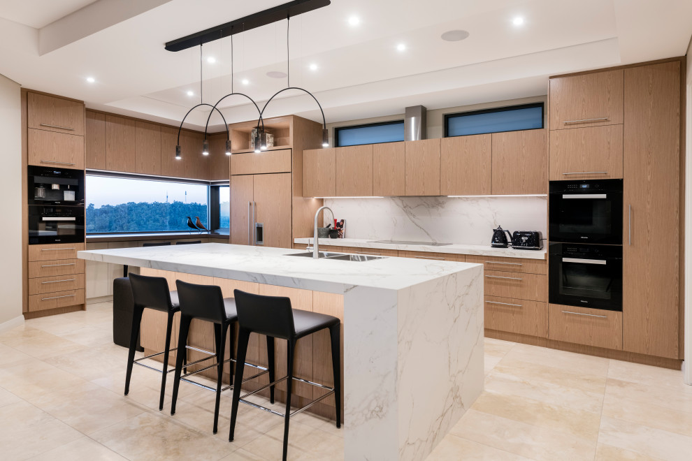 Design ideas for a large contemporary l-shaped open plan kitchen in Perth with a double-bowl sink, recessed-panel cabinets, light wood cabinets, white splashback, black appliances, travertine floors, with island, beige floor and white benchtop.