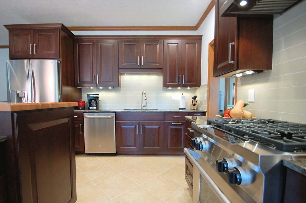 Inspiration for a large transitional l-shaped eat-in kitchen remodel in Columbus with an undermount sink, raised-panel cabinets, dark wood cabinets, granite countertops, gray backsplash, ceramic backsplash, stainless steel appliances and an island