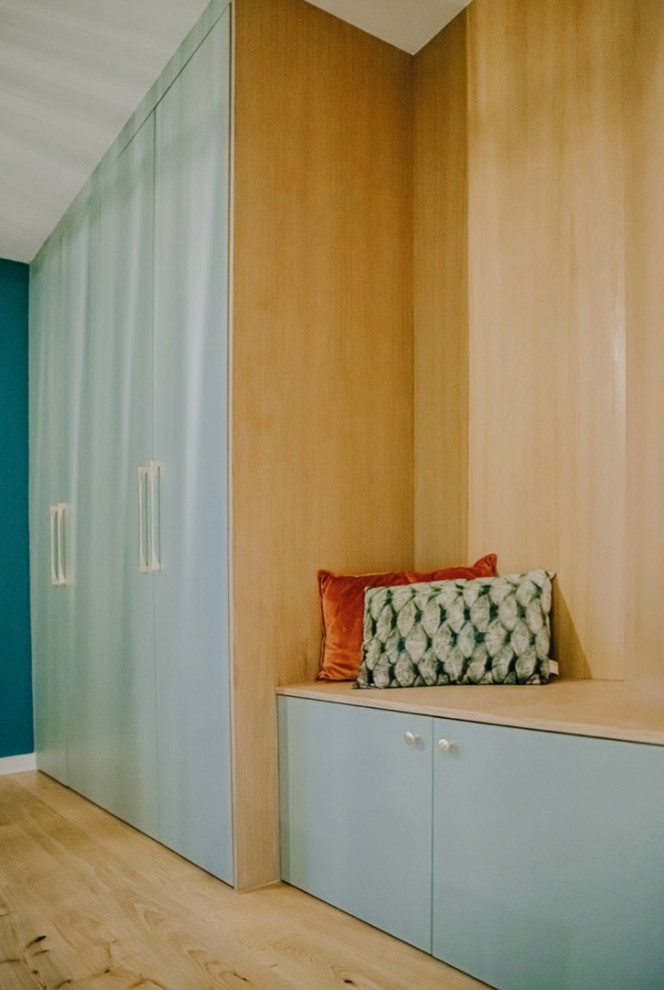 This is an example of a large contemporary gender-neutral dressing room in Lyon with beaded inset cabinets, blue cabinets and light hardwood floors.