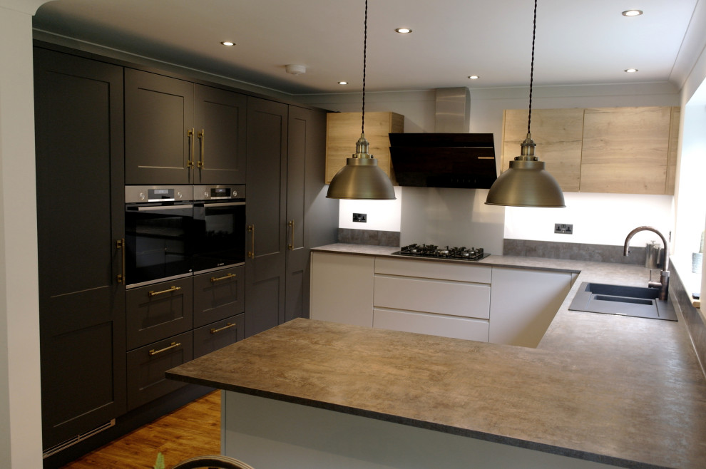 Design ideas for a mid-sized eclectic u-shaped eat-in kitchen in Other with a double-bowl sink, shaker cabinets, grey cabinets, laminate benchtops, grey splashback, glass sheet splashback, black appliances, medium hardwood floors, a peninsula, brown floor and grey benchtop.