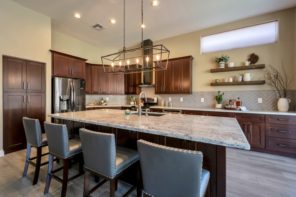 Open concept kitchen - mid-sized transitional l-shaped porcelain tile and brown floor open concept kitchen idea in Phoenix with a single-bowl sink, shaker cabinets, brown cabinets, granite countertops, gray backsplash, brick backsplash, stainless steel appliances, an island and multicolored countertops