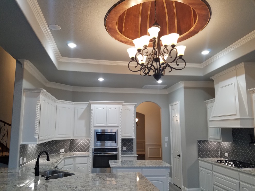 Photo of a large traditional l-shaped open plan kitchen in Dallas with a double-bowl sink, raised-panel cabinets, white cabinets, granite benchtops, grey splashback, porcelain splashback, stainless steel appliances, dark hardwood floors, with island, brown floor and grey benchtop.