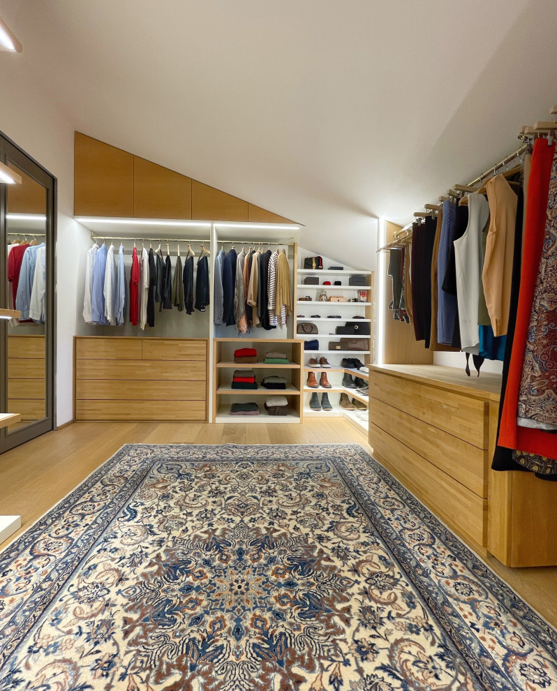 Photo of an expansive contemporary gender neutral walk-in wardrobe in Bologna with open cabinets, light wood cabinets and light hardwood flooring.