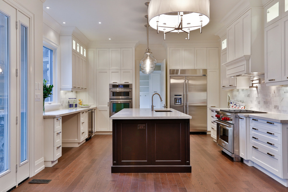 This is an example of a large transitional u-shaped kitchen pantry in Toronto with an undermount sink, shaker cabinets, white cabinets, quartzite benchtops, white splashback, mosaic tile splashback, stainless steel appliances, light hardwood floors and with island.