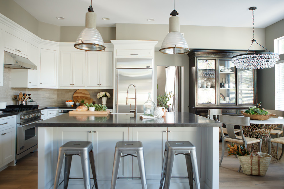 Inspiration for a large transitional l-shaped eat-in kitchen in Orange County with a farmhouse sink, shaker cabinets, white cabinets, beige splashback, stone tile splashback, stainless steel appliances, light hardwood floors and with island.
