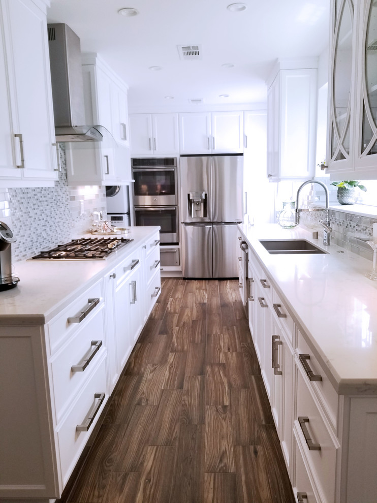 Photo of a small traditional galley separate kitchen in Los Angeles with an undermount sink, recessed-panel cabinets, white cabinets, quartz benchtops, grey splashback, glass tile splashback, stainless steel appliances, porcelain floors, no island and brown floor.