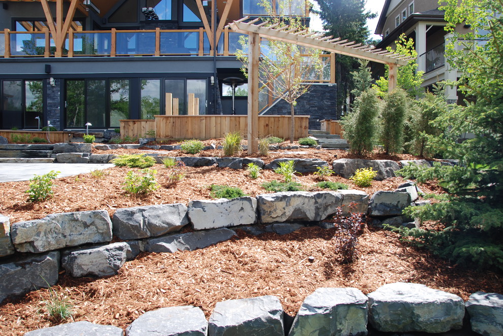 Design ideas for a large contemporary backyard full sun garden in Calgary with a retaining wall and natural stone pavers.