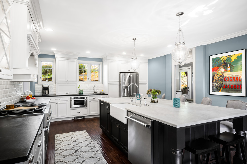 This is an example of a large traditional l-shaped eat-in kitchen in Philadelphia with a farmhouse sink, recessed-panel cabinets, marble benchtops, white splashback, subway tile splashback, stainless steel appliances, dark hardwood floors, with island and white cabinets.