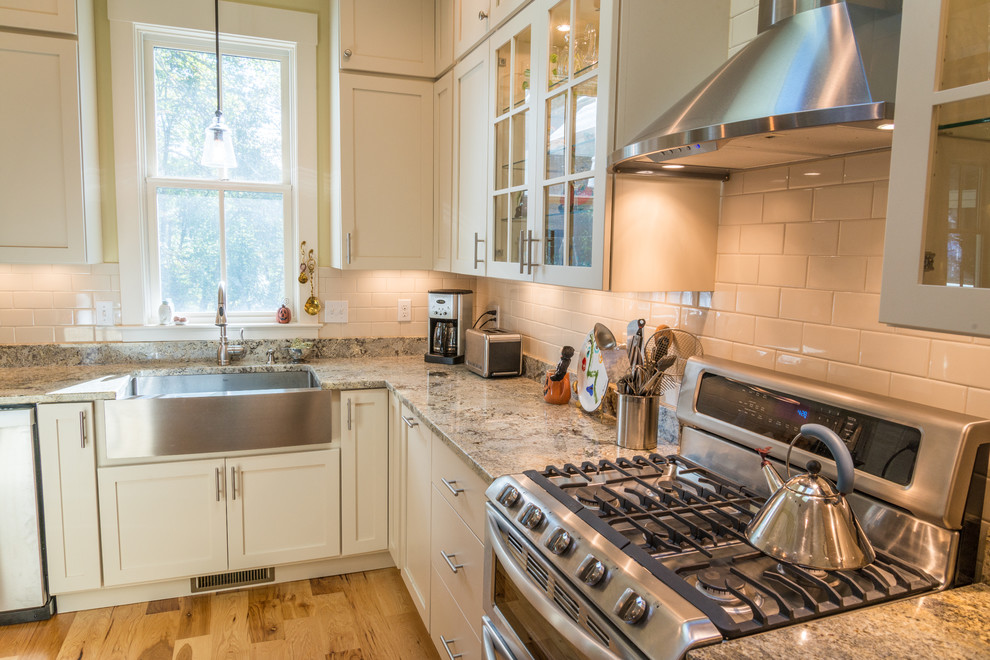 This is an example of a country kitchen in Other with a farmhouse sink, recessed-panel cabinets, white cabinets, white splashback, subway tile splashback and stainless steel appliances.