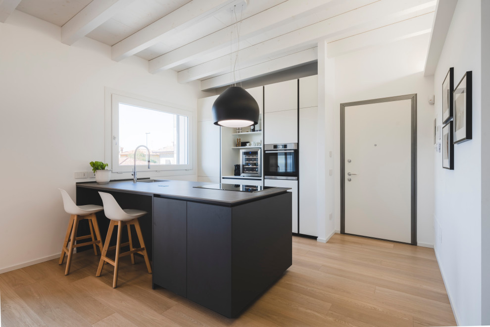 Photo of a mid-sized scandinavian galley open plan kitchen in Milan with an undermount sink, flat-panel cabinets, white cabinets, solid surface benchtops, stainless steel appliances, with island, beige floor, grey benchtop, wood and light hardwood floors.