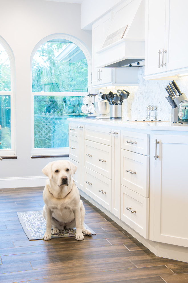 Large transitional u-shaped porcelain tile and brown floor eat-in kitchen photo with an undermount sink, shaker cabinets, white cabinets, quartz countertops, white backsplash, marble backsplash, stainless steel appliances and two islands
