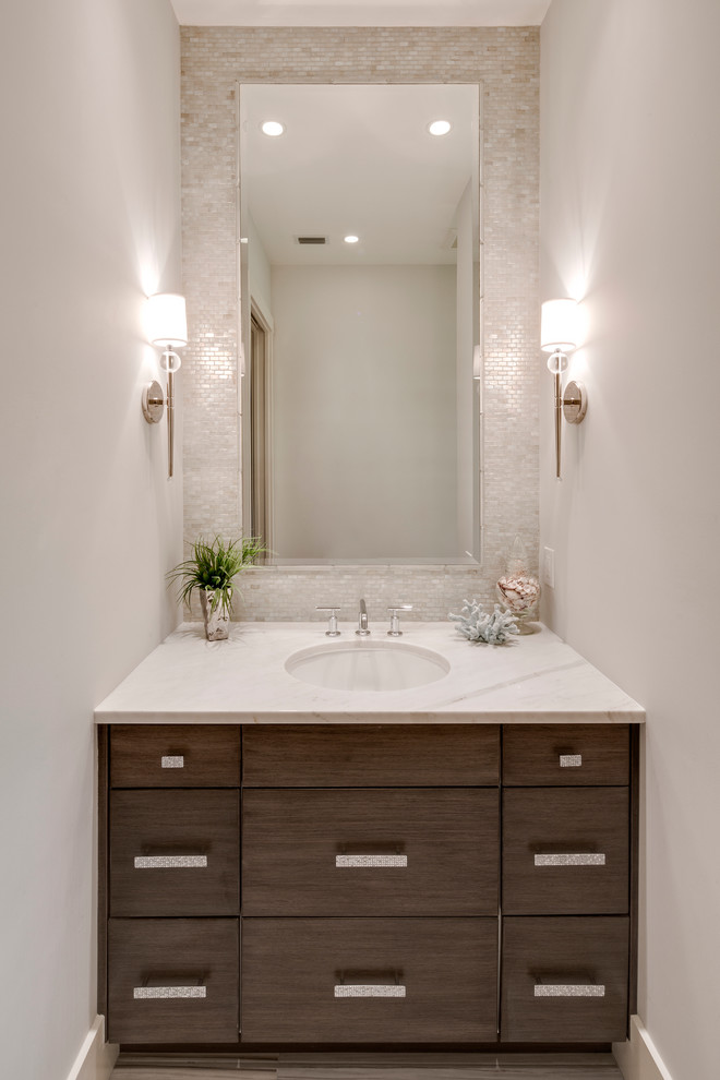 This is an example of a beach style powder room in Miami with an undermount sink, flat-panel cabinets, dark wood cabinets, engineered quartz benchtops, gray tile, mosaic tile, white walls and white benchtops.