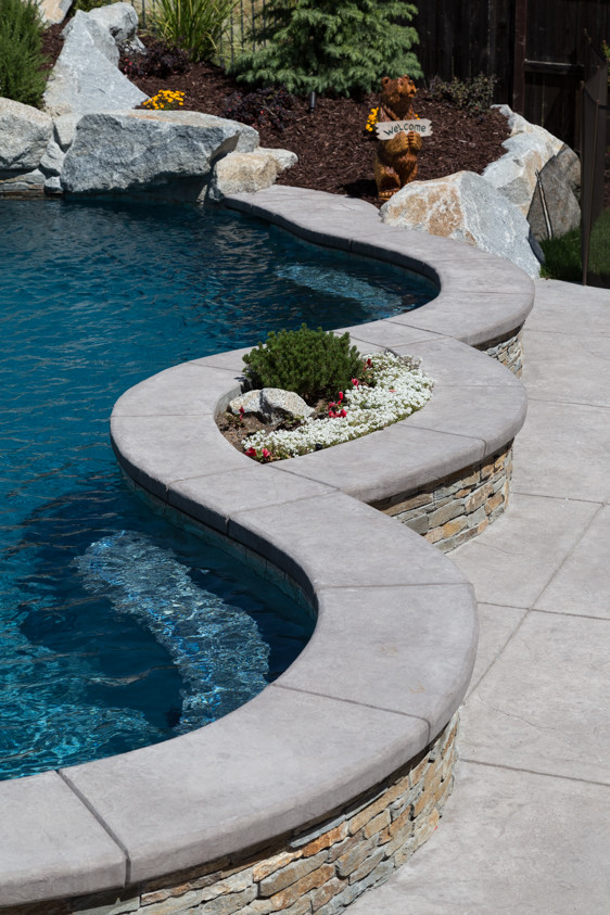 This is an example of a large tropical backyard custom-shaped pool in Sacramento with a water slide and stamped concrete.