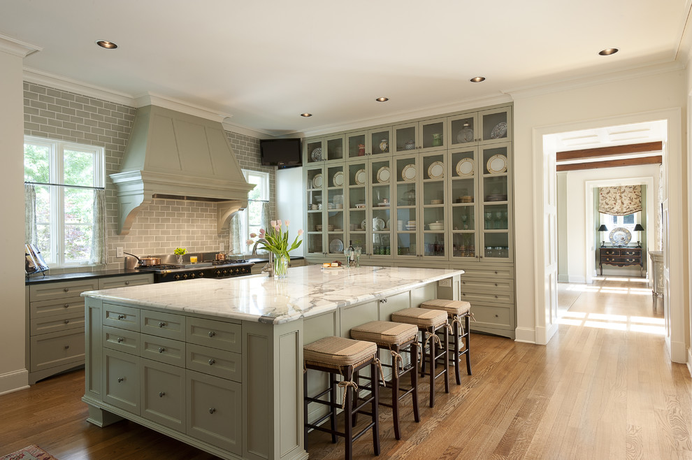 Mid-sized traditional u-shaped separate kitchen in Dallas with glass-front cabinets, subway tile splashback, green cabinets, a farmhouse sink, marble benchtops, grey splashback, medium hardwood floors and with island.