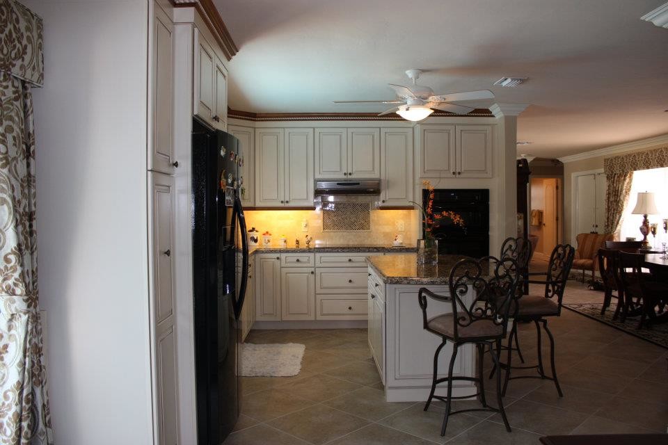 Mid-sized traditional l-shaped eat-in kitchen in Miami with an undermount sink, raised-panel cabinets, white cabinets, granite benchtops, beige splashback, stone tile splashback, black appliances, porcelain floors and with island.