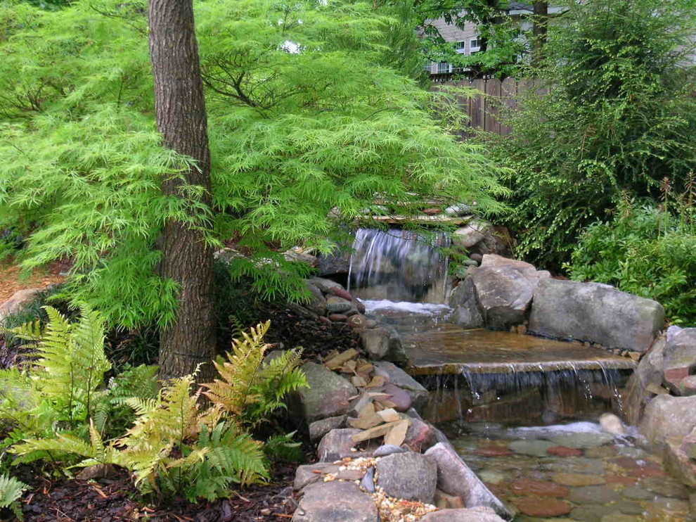 Inspiration for a large traditional backyard custom-shaped natural pool in Atlanta with a water feature and natural stone pavers.