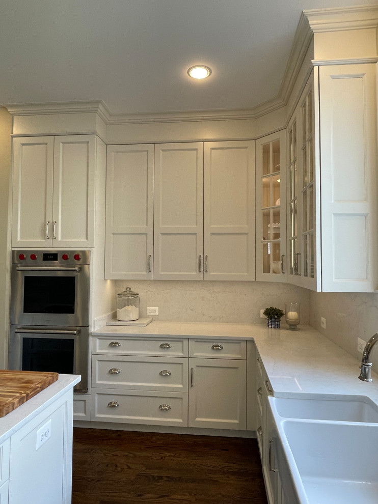 Mid-sized u-shaped medium tone wood floor and brown floor eat-in kitchen photo in DC Metro with a farmhouse sink, shaker cabinets, white cabinets, quartz countertops, white backsplash, quartz backsplash, stainless steel appliances, an island and white countertops