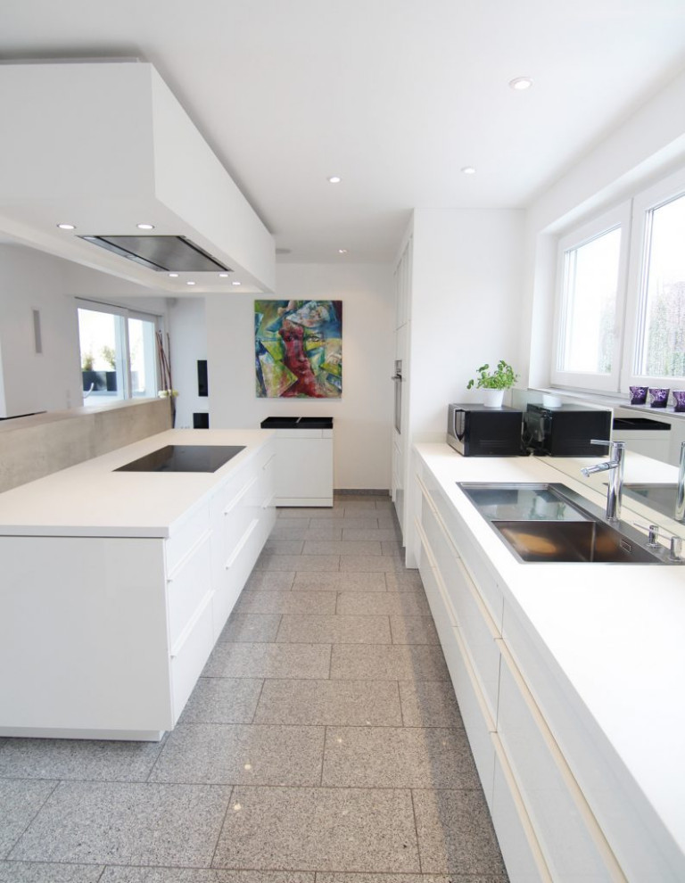 This is an example of a large modern galley kitchen in Other with an integrated sink, flat-panel cabinets, white cabinets, wood benchtops, white splashback, black appliances, no island, grey floor and white benchtop.