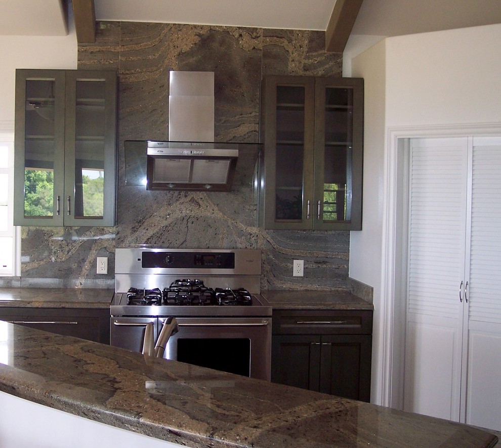 Photo of a mid-sized transitional l-shaped open plan kitchen in Hawaii with an undermount sink, recessed-panel cabinets, brown cabinets, granite benchtops, brown splashback, stone slab splashback, stainless steel appliances, with island, brown benchtop, travertine floors and beige floor.