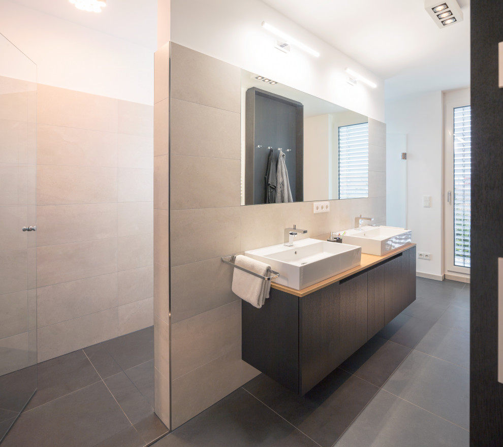 Photo of a modern ensuite bathroom in Munich with flat-panel cabinets, black cabinets, a built-in shower, stone tiles, a vessel sink, solid surface worktops, an open shower, double sinks, a freestanding bath, light hardwood flooring, white worktops and a freestanding vanity unit.