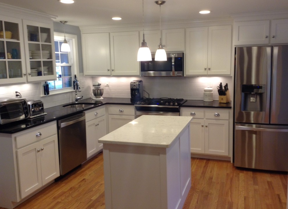 Mid-sized transitional l-shaped medium tone wood floor and brown floor kitchen photo in New York with an undermount sink, shaker cabinets, white cabinets, granite countertops, white backsplash, subway tile backsplash, stainless steel appliances and an island