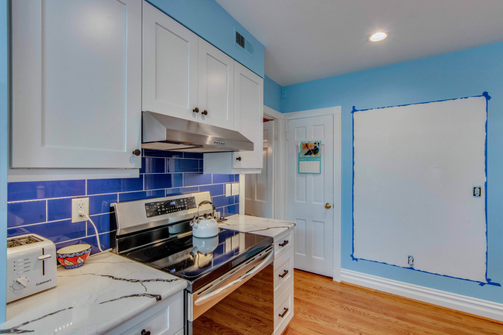 Foto på ett litet vintage vit kök, med en trippel diskho, skåp i shakerstil, vita skåp, bänkskiva i kvarts, blått stänkskydd, stänkskydd i tunnelbanekakel, rostfria vitvaror, mellanmörkt trägolv, en halv köksö och brunt golv