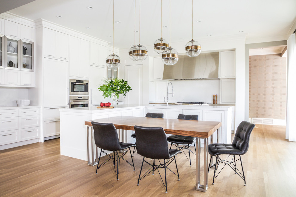Inspiration for a transitional l-shaped medium tone wood floor and brown floor eat-in kitchen remodel in Calgary with shaker cabinets, white cabinets, white backsplash, stainless steel appliances, an island and white countertops