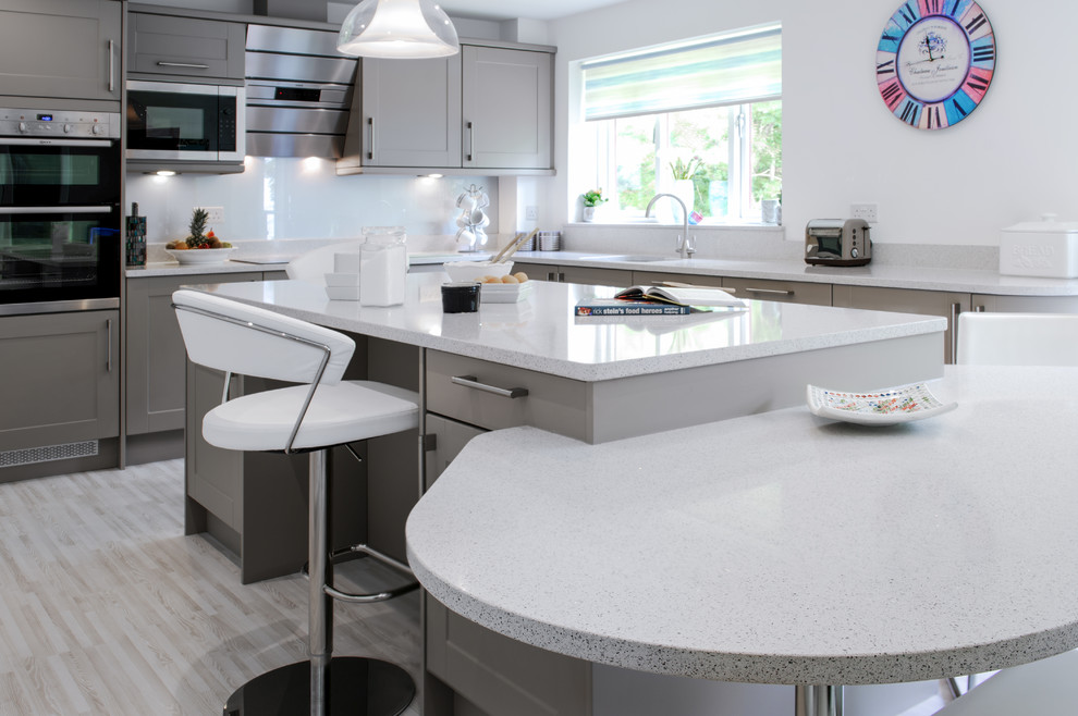 Design ideas for a mid-sized contemporary l-shaped eat-in kitchen in Cornwall with a farmhouse sink, shaker cabinets, beige cabinets, granite benchtops, blue splashback, glass sheet splashback and with island.
