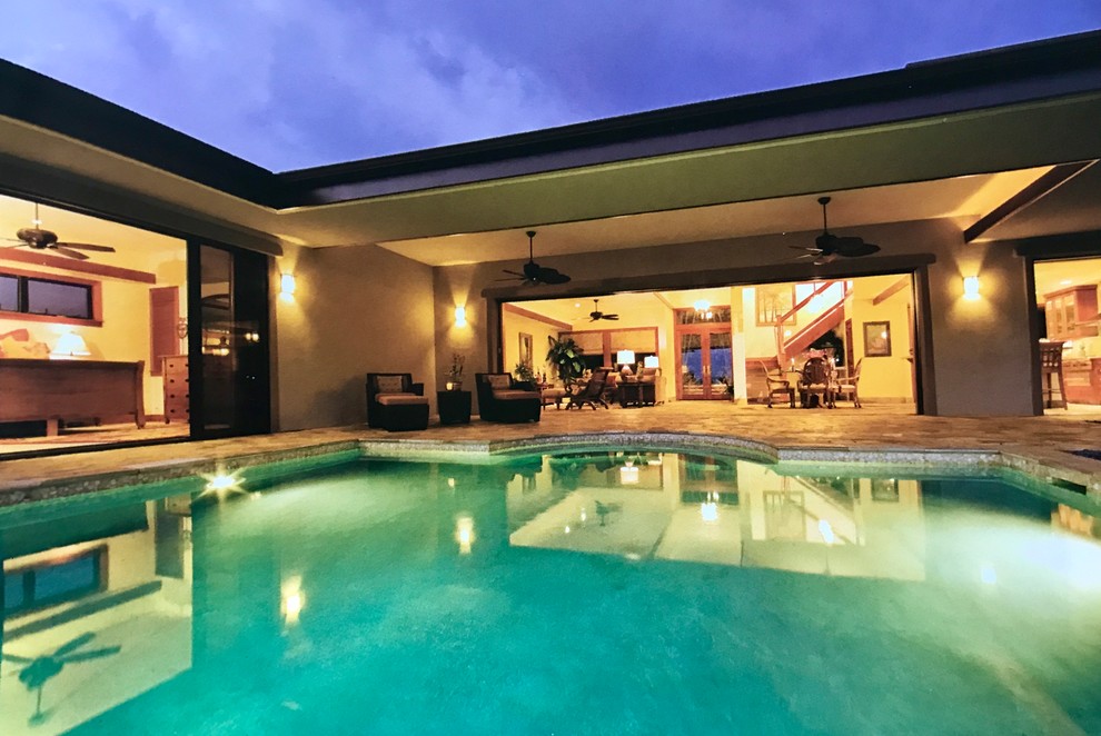Inspiration for a large tropical backyard custom-shaped infinity pool in Hawaii with natural stone pavers.