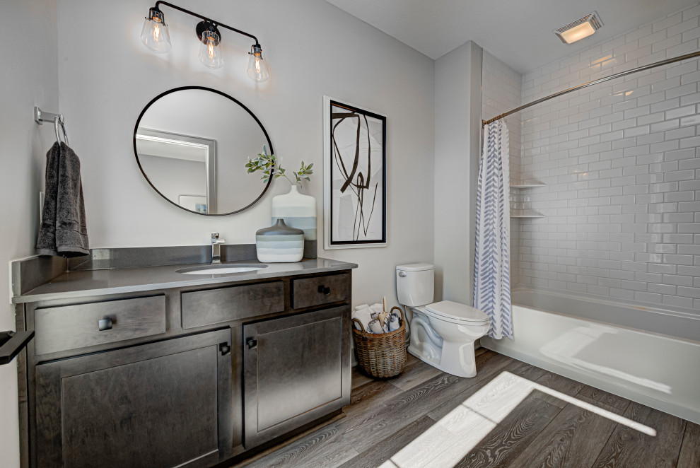 Photo of a mid-sized contemporary master bathroom in Indianapolis with shaker cabinets, a corner tub, a shower/bathtub combo, a one-piece toilet, grey walls, an undermount sink, engineered quartz benchtops, a shower curtain, grey benchtops, a single vanity, a built-in vanity, distressed cabinets, white tile, subway tile, medium hardwood floors, brown floor and an enclosed toilet.