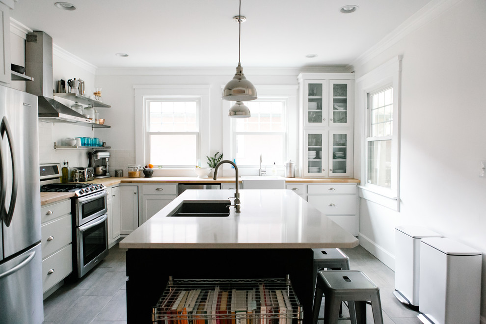 Design ideas for a transitional l-shaped kitchen in Indianapolis with a farmhouse sink, white cabinets, wood benchtops, white splashback, stainless steel appliances and subway tile splashback.