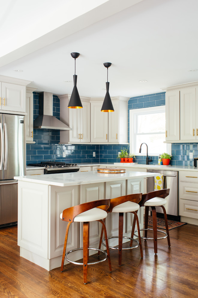 Photo of a mid-sized transitional l-shaped kitchen in New York with raised-panel cabinets, white cabinets, blue splashback, subway tile splashback, stainless steel appliances, medium hardwood floors, with island and white benchtop.