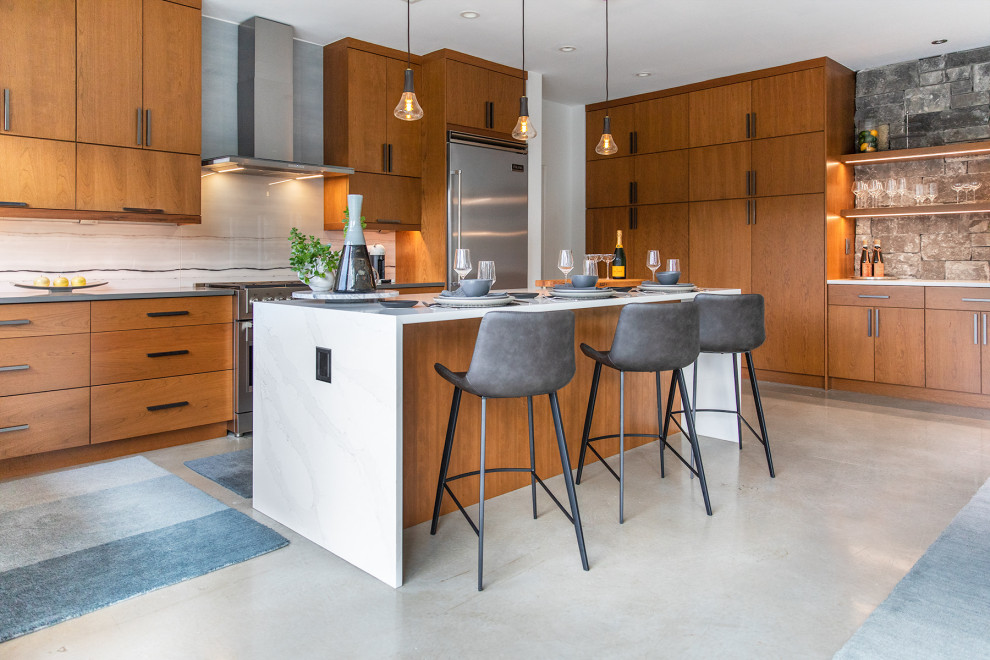 This is an example of a midcentury l-shaped kitchen in Austin with flat-panel cabinets, medium wood cabinets, white splashback, stainless steel appliances, with island, grey floor and white benchtop.