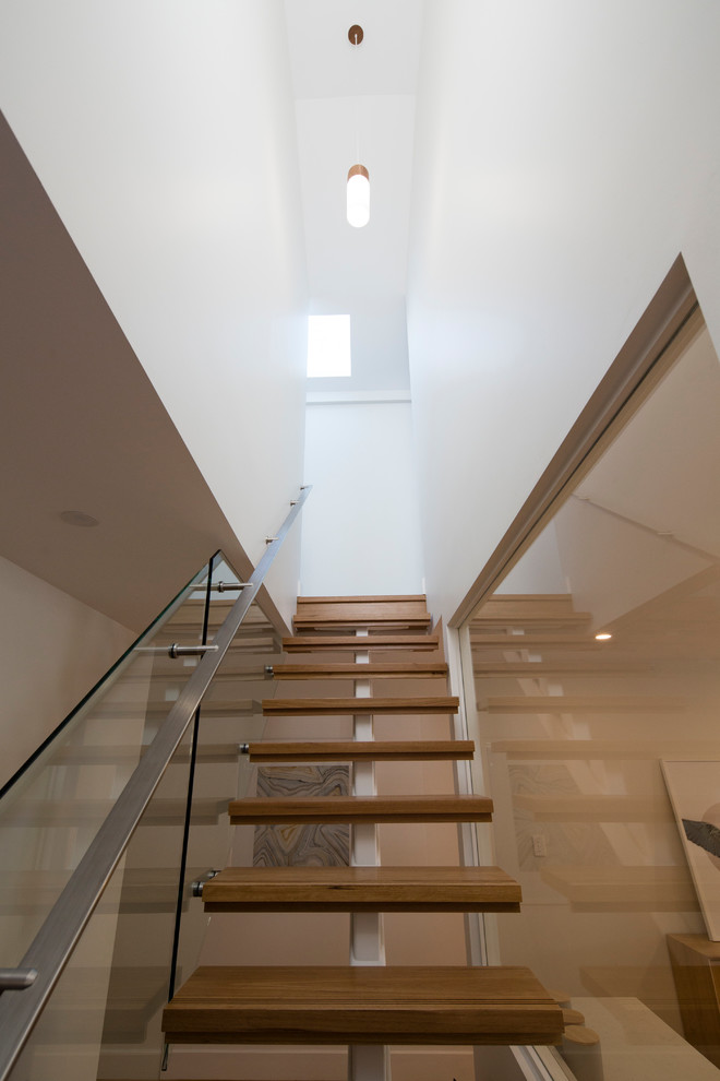 This is an example of a mid-sized contemporary wood straight staircase in Sydney with metal risers and glass railing.