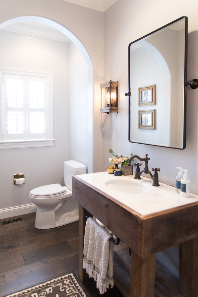 Country powder room in St Louis with furniture-like cabinets, dark wood cabinets, a two-piece toilet, grey walls, dark hardwood floors, an undermount sink, brown floor and white benchtops.