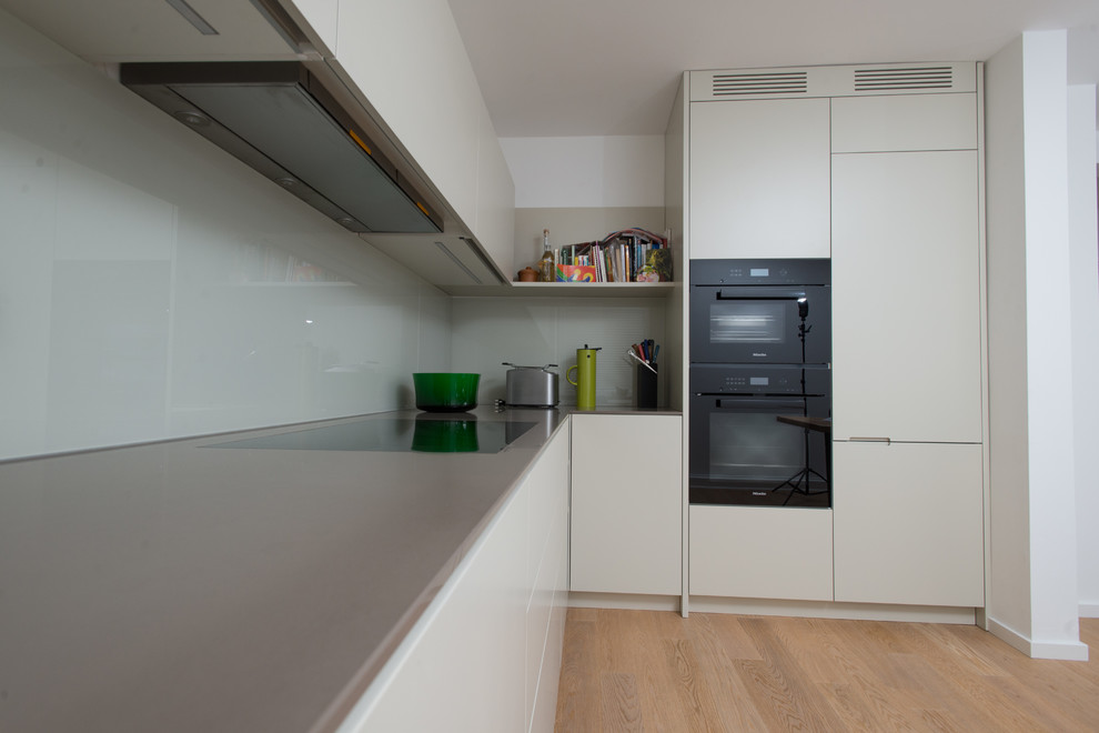 Inspiration for a mid-sized contemporary l-shaped separate kitchen in Munich with an integrated sink, flat-panel cabinets, beige cabinets, wood benchtops, white splashback, glass sheet splashback, stainless steel appliances, dark hardwood floors, no island and brown floor.