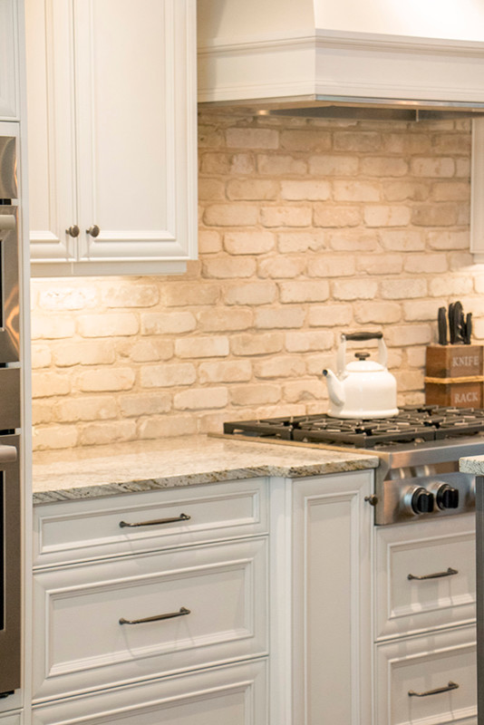 Example of a large transitional l-shaped eat-in kitchen design with a double-bowl sink, shaker cabinets, white cabinets, beige backsplash, stainless steel appliances and an island