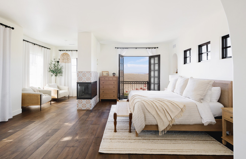 This is an example of a mediterranean bedroom in San Luis Obispo with white walls, dark hardwood floors, a corner fireplace and brown floor.