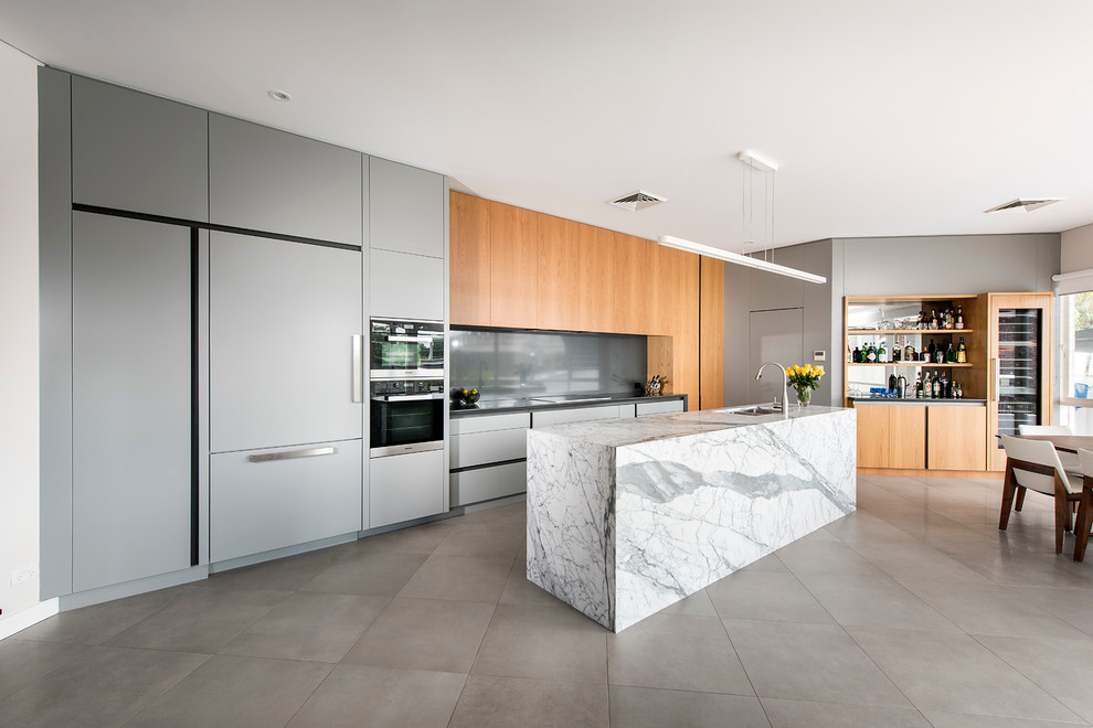 Inspiration for a mid-sized contemporary open plan kitchen in Perth with a drop-in sink, recessed-panel cabinets, grey cabinets, solid surface benchtops, grey splashback, glass sheet splashback, stainless steel appliances, porcelain floors and with island.