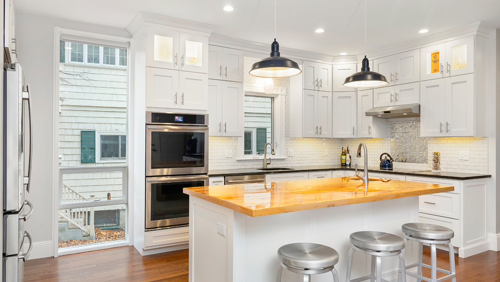 Inspiration for a mid-sized transitional u-shaped kitchen in Boston with an undermount sink, shaker cabinets, white cabinets, wood benchtops, white splashback, subway tile splashback, stainless steel appliances, medium hardwood floors, with island, brown floor and brown benchtop.