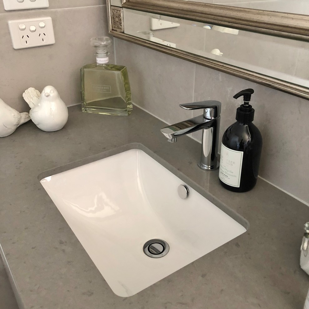 Inspiration for a mid-sized contemporary master bathroom with furniture-like cabinets, white cabinets, a corner tub, an open shower, a one-piece toilet, gray tile, ceramic tile, grey walls, ceramic floors, an undermount sink, solid surface benchtops, grey floor and grey benchtops.