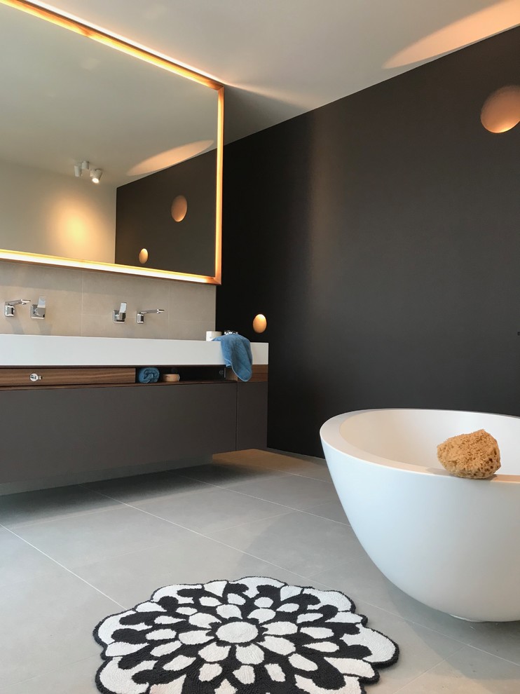 Photo of a mid-sized modern master bathroom in Munich with flat-panel cabinets, dark wood cabinets, a freestanding tub, a curbless shower, a wall-mount toilet, gray tile, ceramic tile, ceramic floors, a vessel sink, solid surface benchtops, grey floor, an open shower and black walls.